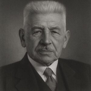 Porträt von Ludwig Aschoff (1866–1942) in Schwarz-Weiss, mit Schnurrbart, kurzem Haar, Anzug und Krawatte, ernster Blick, neutraler Hintergrund.